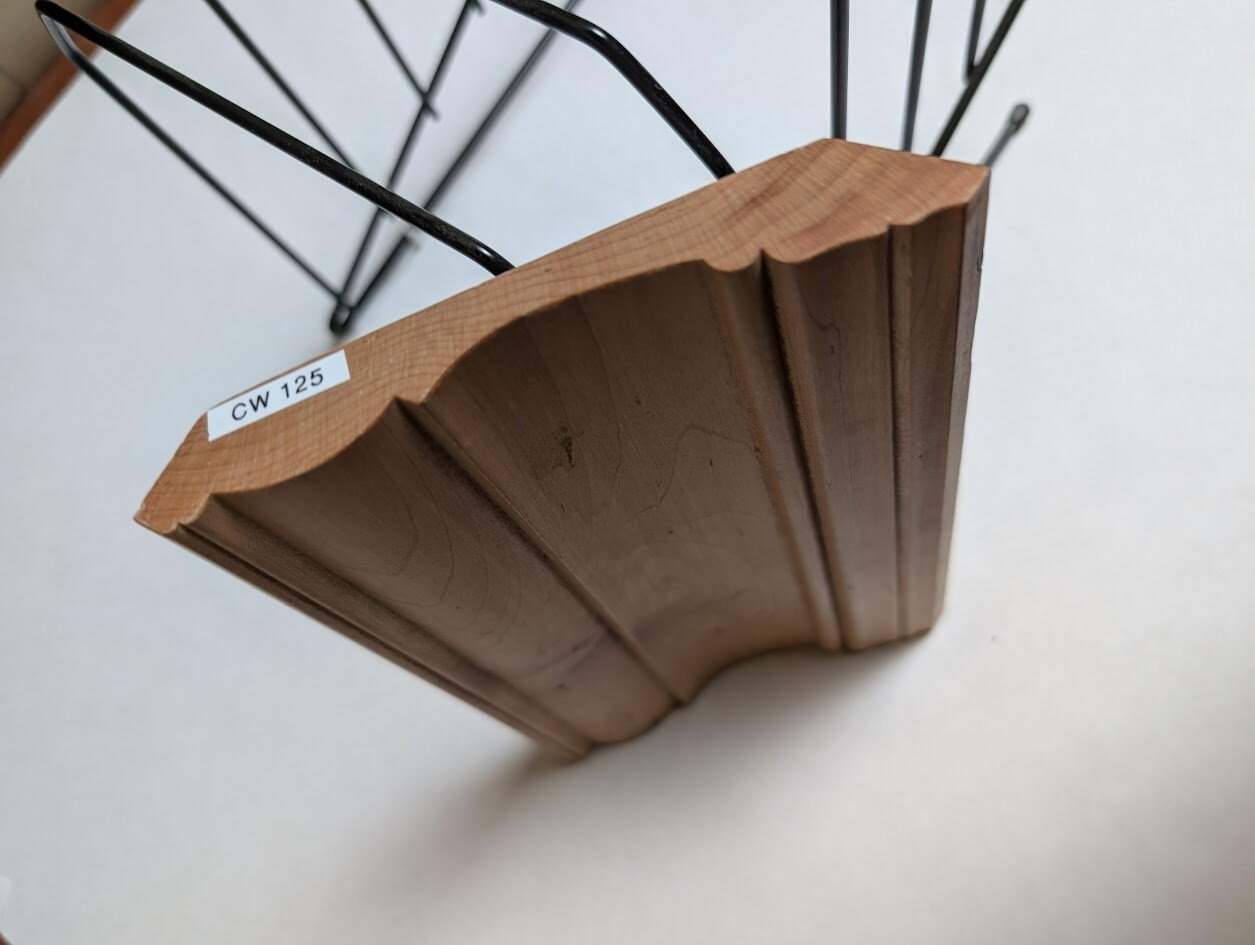 A wooden molding sample with a decorative edge, labeled CW 125, is displayed upright in a metal stand against a white background—perfect inspiration from bespoke cabinetry manufacturers and cabinet makers in Honey Brook, PA.