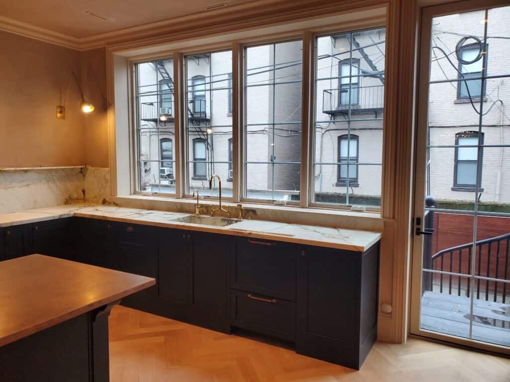 Elegant black custom kitchen cabinets with marble countertops and large window for natural light.